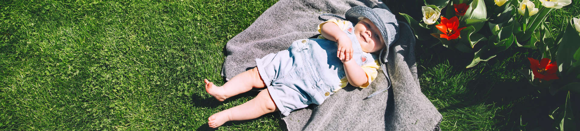 happy baby lying on a blanket placed on well-maintained grass in the garden