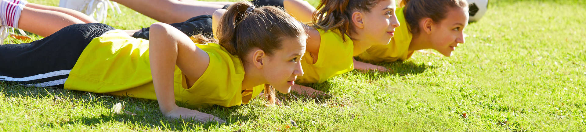 teenage girls doing push ups for warm-up on a football pitch