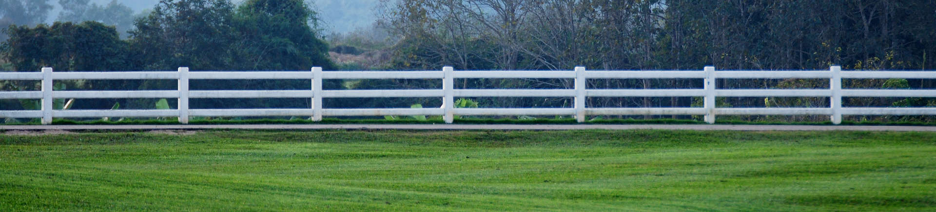 well-maintained grass area surrounded with white wooden fence