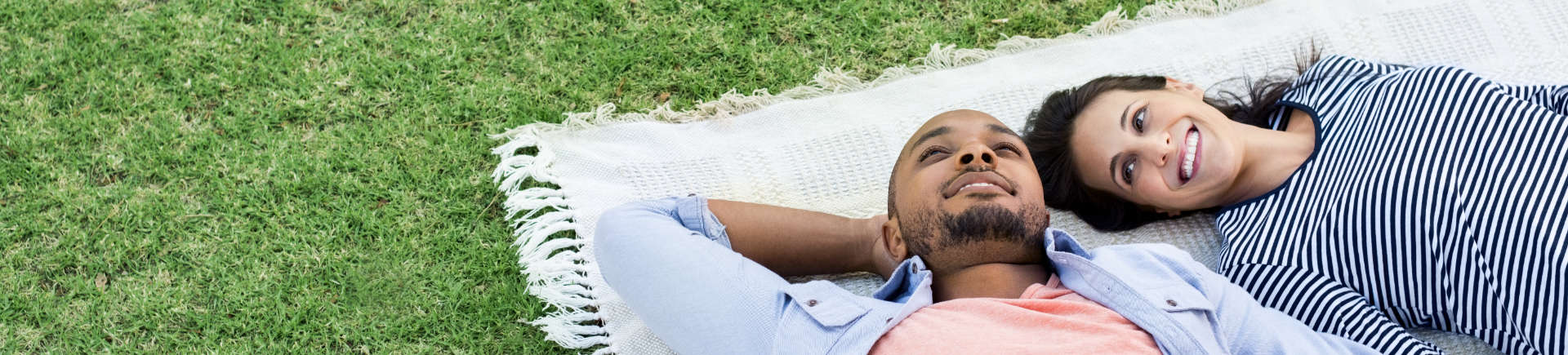 young couple lying on their backs on a blanket stretched on grass in park